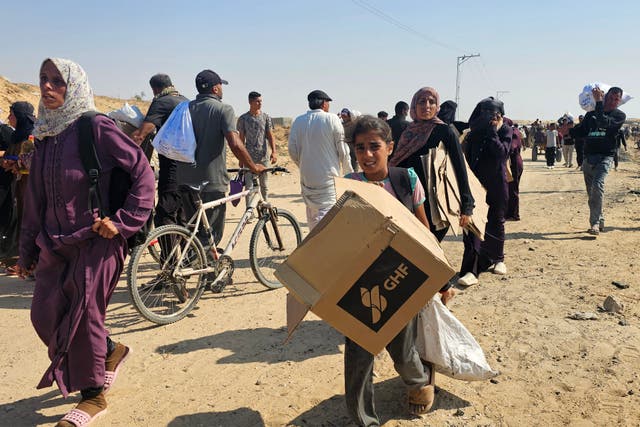 <p>Displaced Palestinians walk along a road to receive humanitarian aid packages from a US-backed foundation in Rafah in the southern Gaza Strip</p>