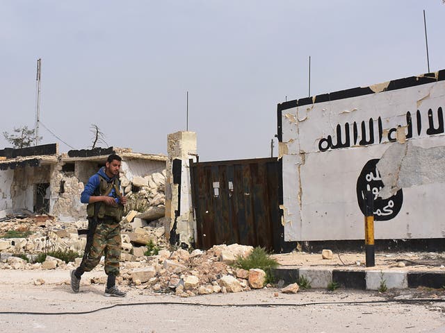 A member of the Syrian government forces walks past Isis graffiti in Syria